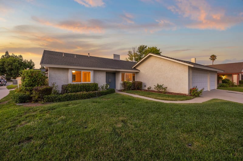 Single story stucco ranch home at twilight with green lawn, hedges and attached two car garage