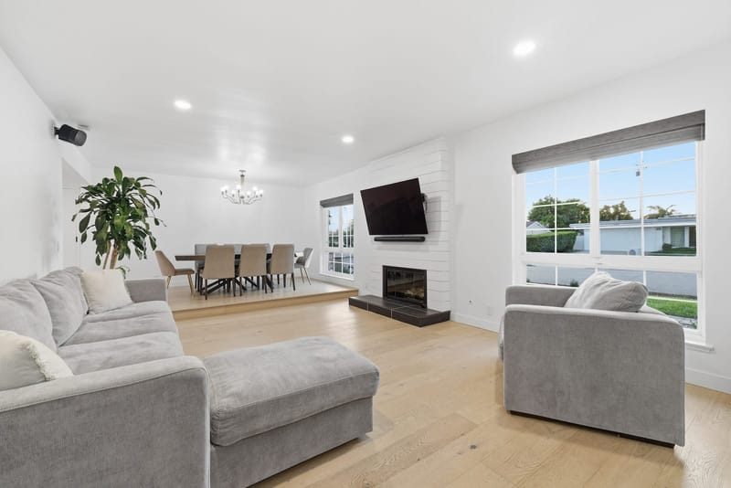 Bright white living room with shiplap fireplace, mounted TV and light oak floors opening to dining area