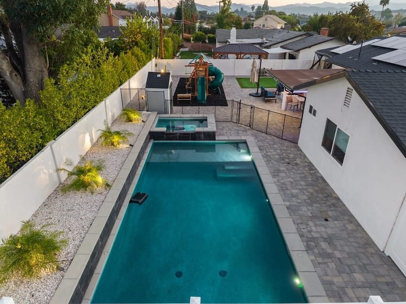 Aerial twilight view of a modern backyard pool and spa with paver patio and playset