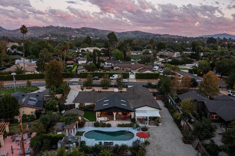 Aerial twilight view of a single story ranch home with kidney shaped pool and rolling hills beyond