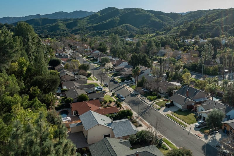 Aerial view of a tree lined suburban neighborhood with green rolling hills in the background