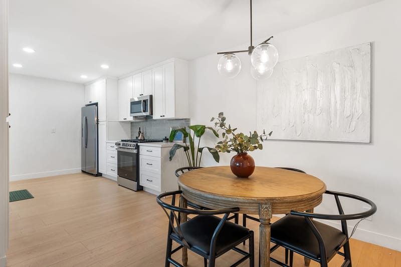 Bright white kitchen with stainless appliances and round wood dining table under globe pendant lights