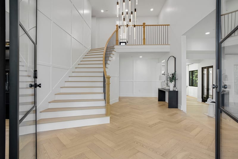 Bright two story entry with curved staircase, herringbone wood floors and modern pendant lights