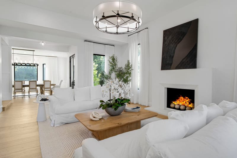 Bright white living room with lit fireplace, slipcovered sofas and oak coffee table