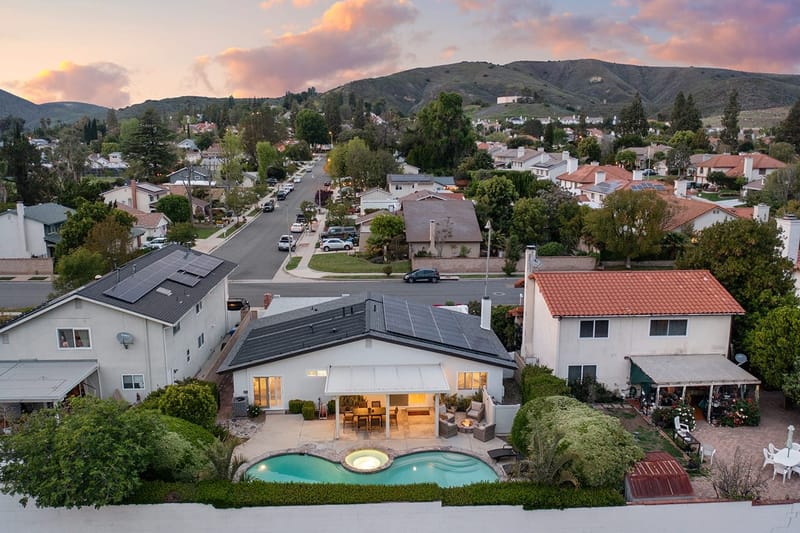 Twilight aerial of a single story home with lit pool and spa in a hillside suburban neighborhood