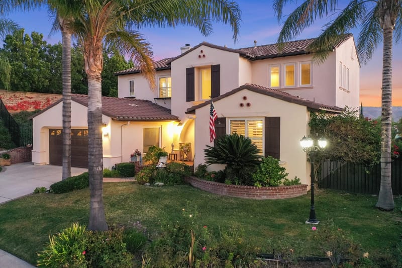 Two story Mediterranean style home at twilight with palm trees and glowing windows