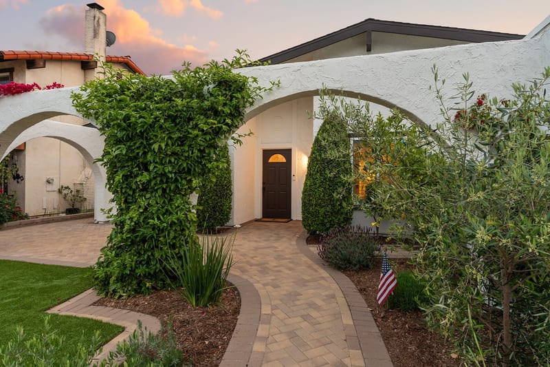 Twilight view of a white stucco Spanish style home entry with arched breezeway and paver walkway