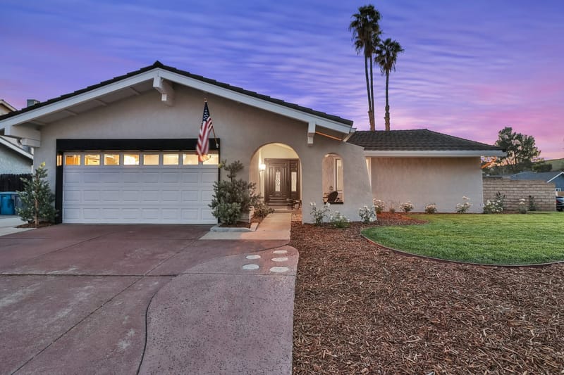 Single story stucco ranch home at twilight with lit entry, lawn and palm trees
