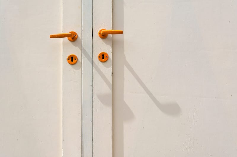 Orange lever handles and keyholes on a sunlit cream painted door with a long shadow