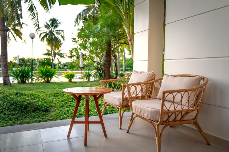 Rattan patio chairs and round wood table on a tiled terrace overlooking palms and a green lawn