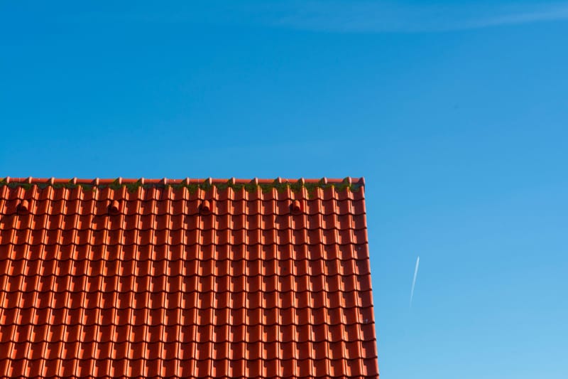 Terracotta tile roofline against a clear blue sky with a distant jet contrail