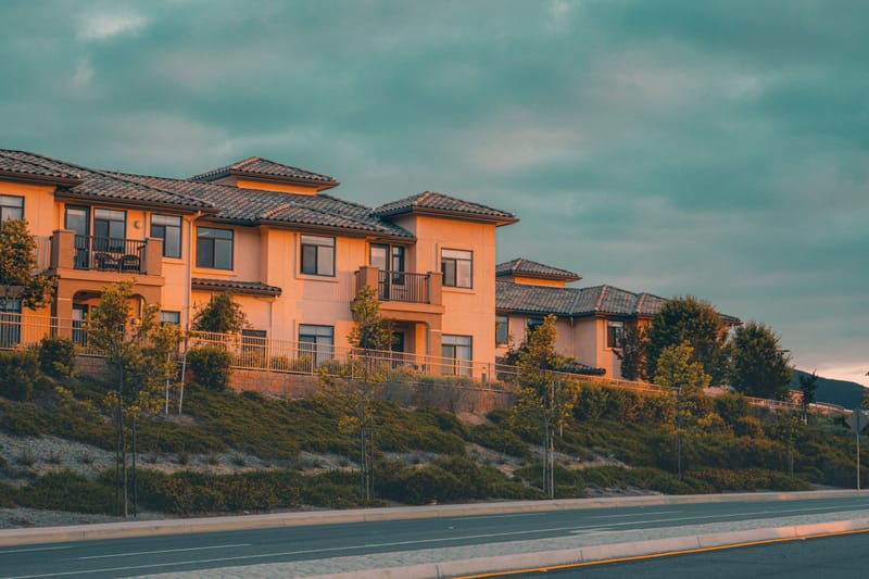 Hillside stucco townhomes with tile roofs glowing in golden sunset light above a California roadway