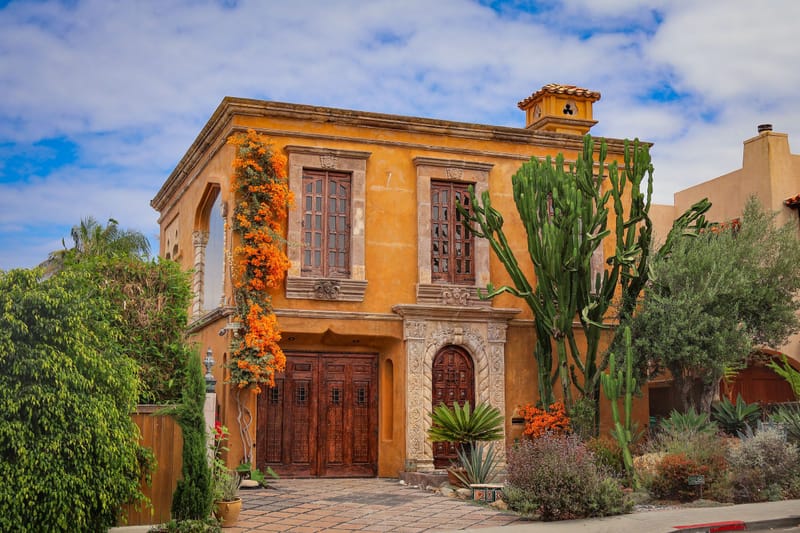 Ochre Spanish style California home with carved wood doors, orange bougainvillea and tall cactus garden.cbd