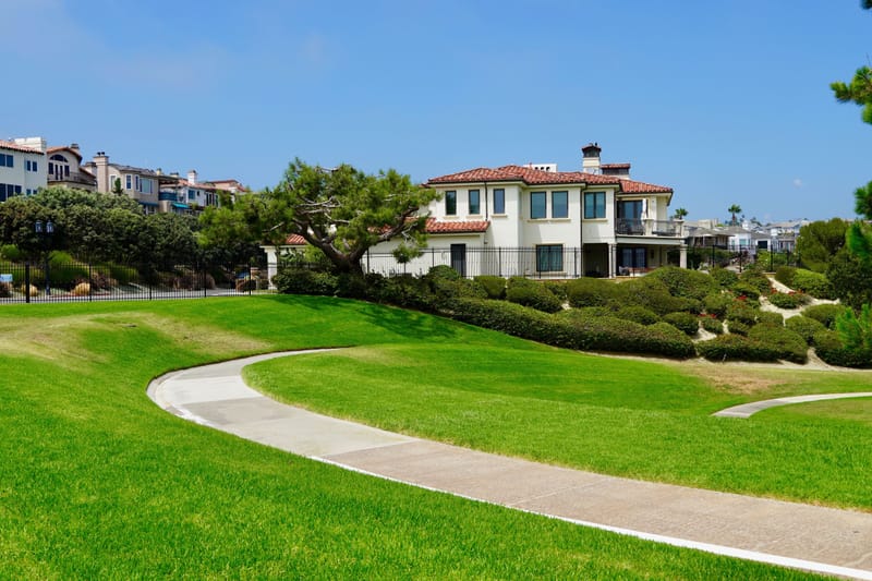 Mediterranean style hillside home overlooking a curving path and manicured green lawn under clear blue sky in coastal California.jpg