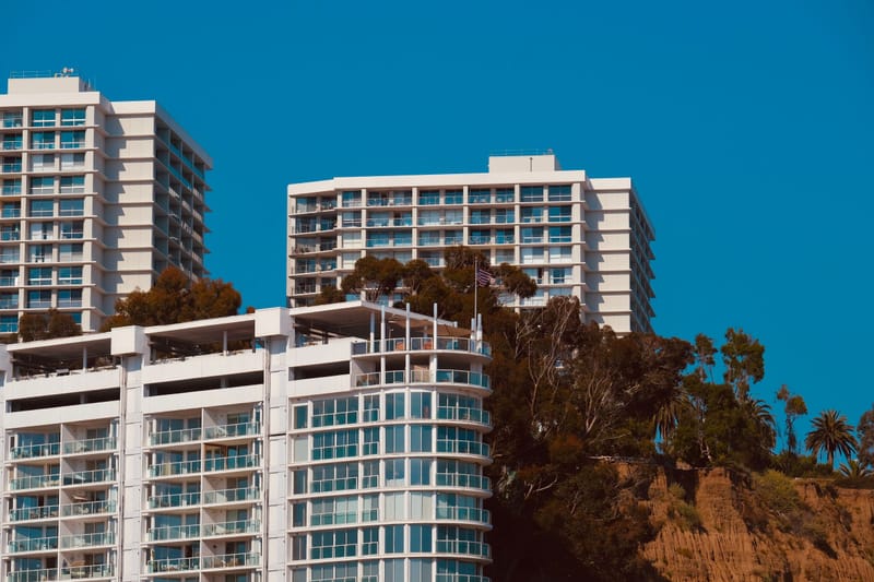 White oceanfront condo towers perched on a bluff above palms under deep blue Southern California sky.ates.ates.ates.
