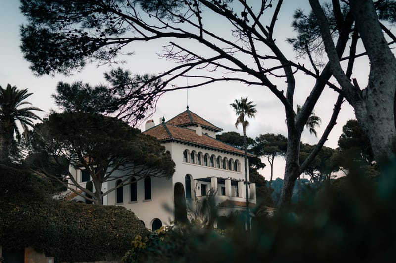 Spanish style villa with terracotta tile roof framed by pines and palms at dusk on a hillside estate.ERROR