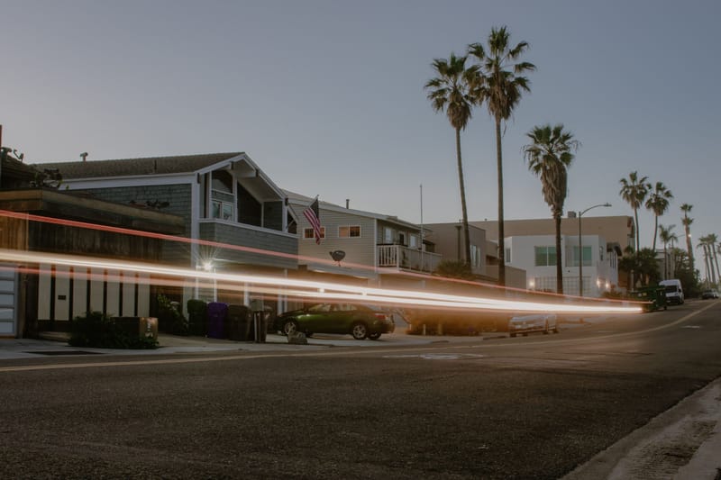 Coastal California street at dusk with palm trees, beach houses and light trails from passing traffic.wi