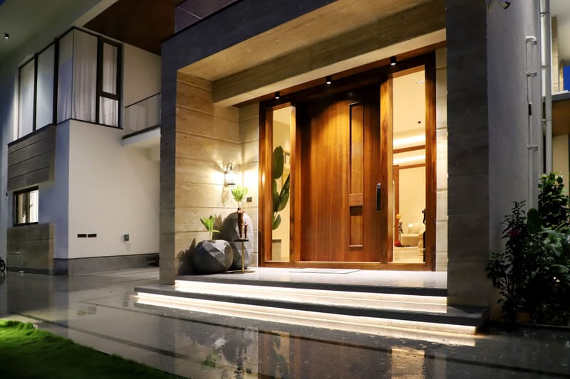 Warmly lit modern home entrance with tall wood door, stone walls and lush plants at dusk.ced steps glisten.ted.g.ed.ful.ive.ry.al.ic.ed.g.y.ic.ed.ly.ed.y.al.ed.ly.ed.y.ed.g.ed.y.al.ed.ly.ed