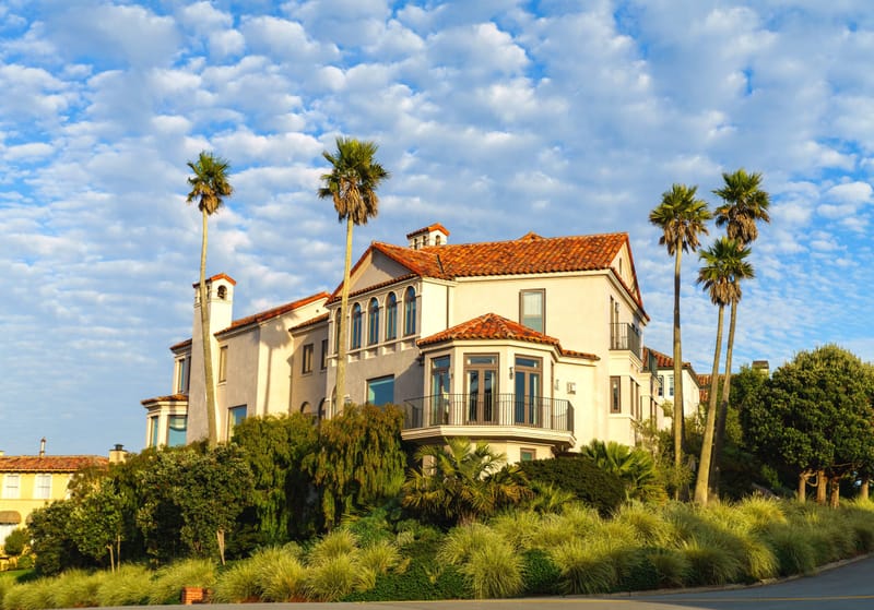 Spanish style hillside estate with red tile roof and palms under a bright blue sky at golden hour