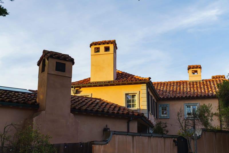 Spanish style home with clay tile roof and stucco chimneys glowing in golden hour light under blue sky.-NO-DASH-
