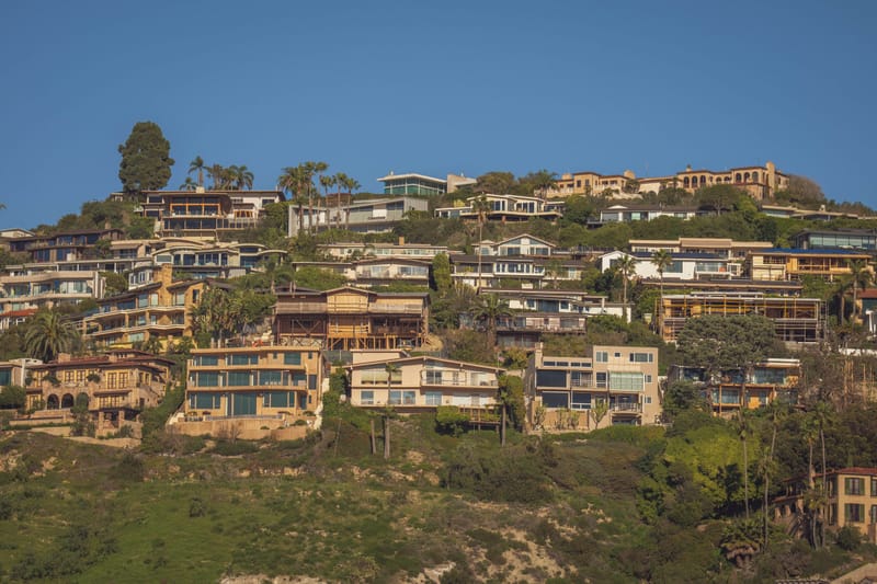 Hillside homes stacked above dry coastal bluff grasses under clear blue Southern California sky','