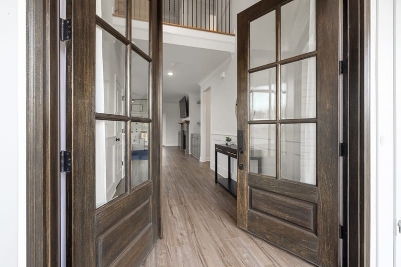 Open dark wood double doors with glass panes leading into a bright entry hall with light oak floors