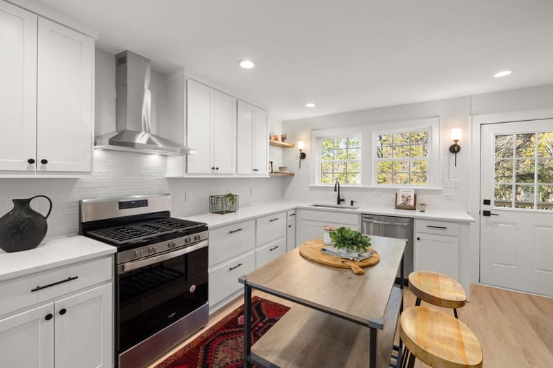 Bright remodeled white kitchen with shaker cabinets, steel range hood, butcher block island and wood stools.wood stools.wood floors.wood counters.wood table.wood trim.wood tone.wood accents.w