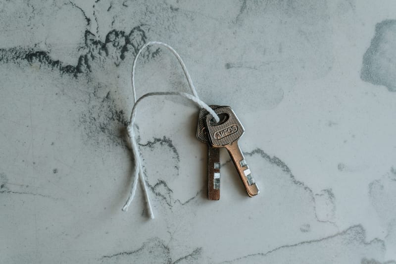 Two brass house keys tied with white string resting on a pale marble surface