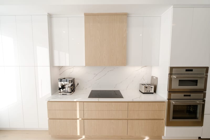 Modern kitchen remodel with white gloss cabinets, light oak drawers and marble backsplash in sunlight