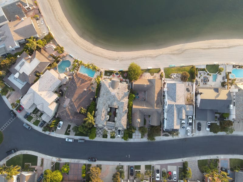 Overhead aerial view of waterfront luxury homes with pools along a sandy beach in Southern California.in